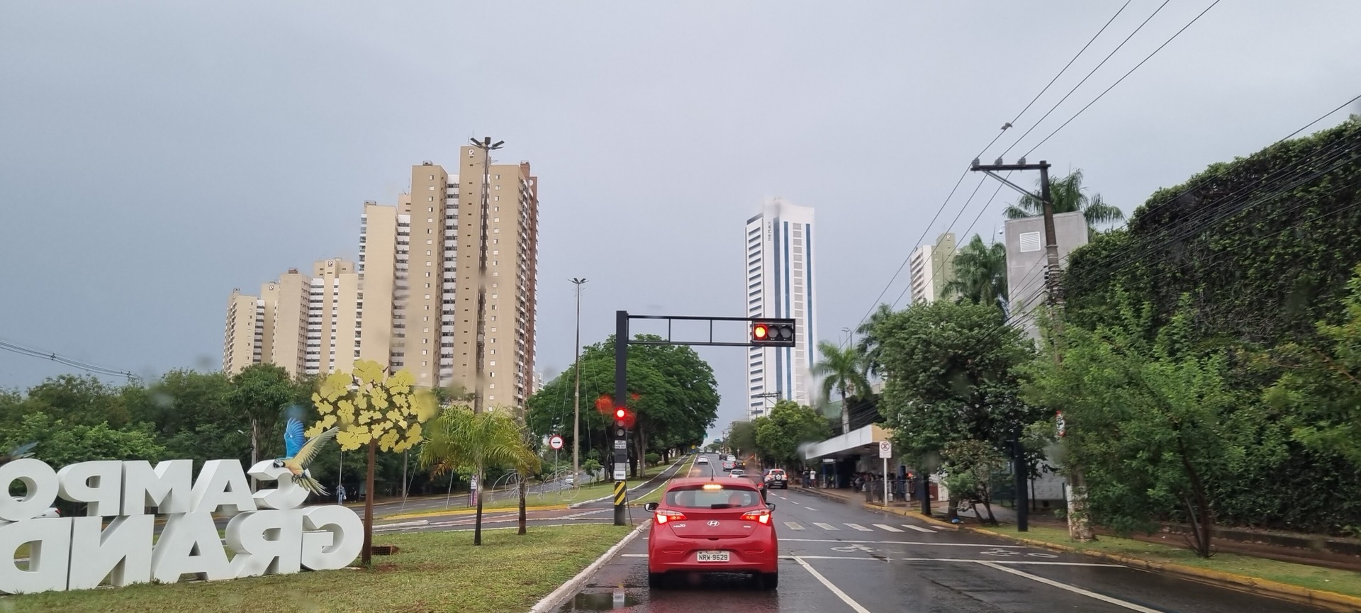 Avenida Afonso Pena, em Campo Grande, com o letreiro da cidade, um carro vermelho e o céu nublado